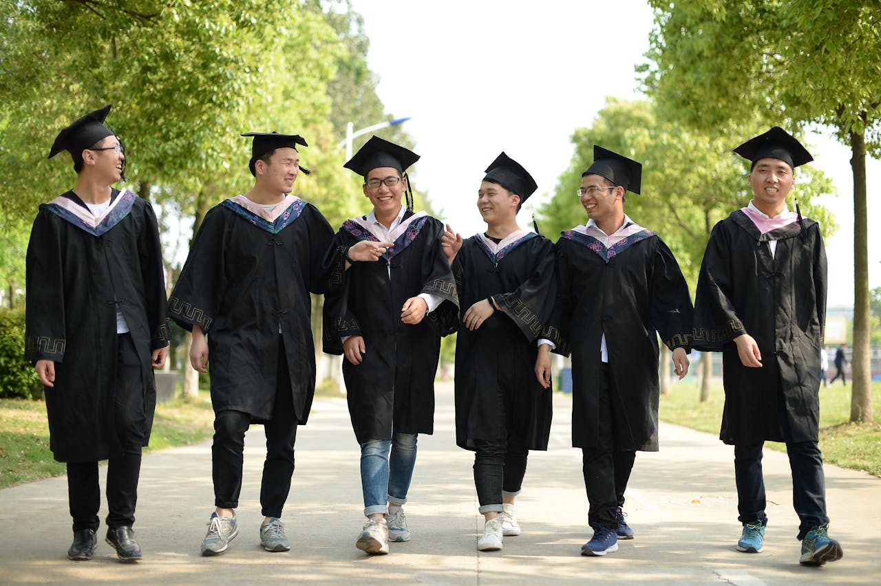 A group of cheerful graduates in caps and gowns walking outside, celebrating their achievement.