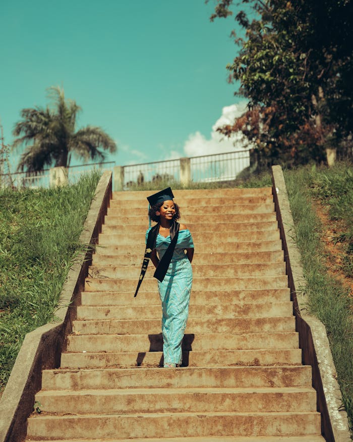 Young woman in graduation attire standing confidently outdoors on steps.