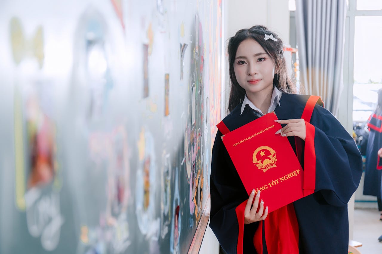 Female graduate in academic gown holding diploma, celebrating achievement indoors.